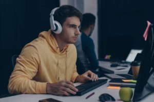 selective focus of programmer in headphones working near african american colleague at night in office