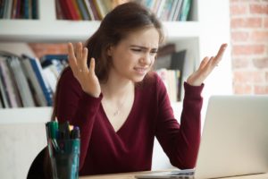 Perplexed female office worker shrugging while looking at laptop screen. Frustrated freelance businesswoman frustrated with confusing email from client, difficult software interface not making sense.