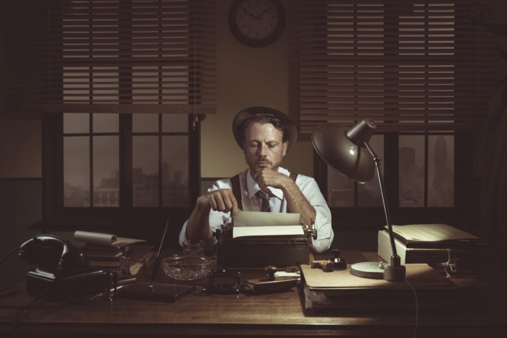 Confident journalist checking errors on text working at his desk, 1950s style office.